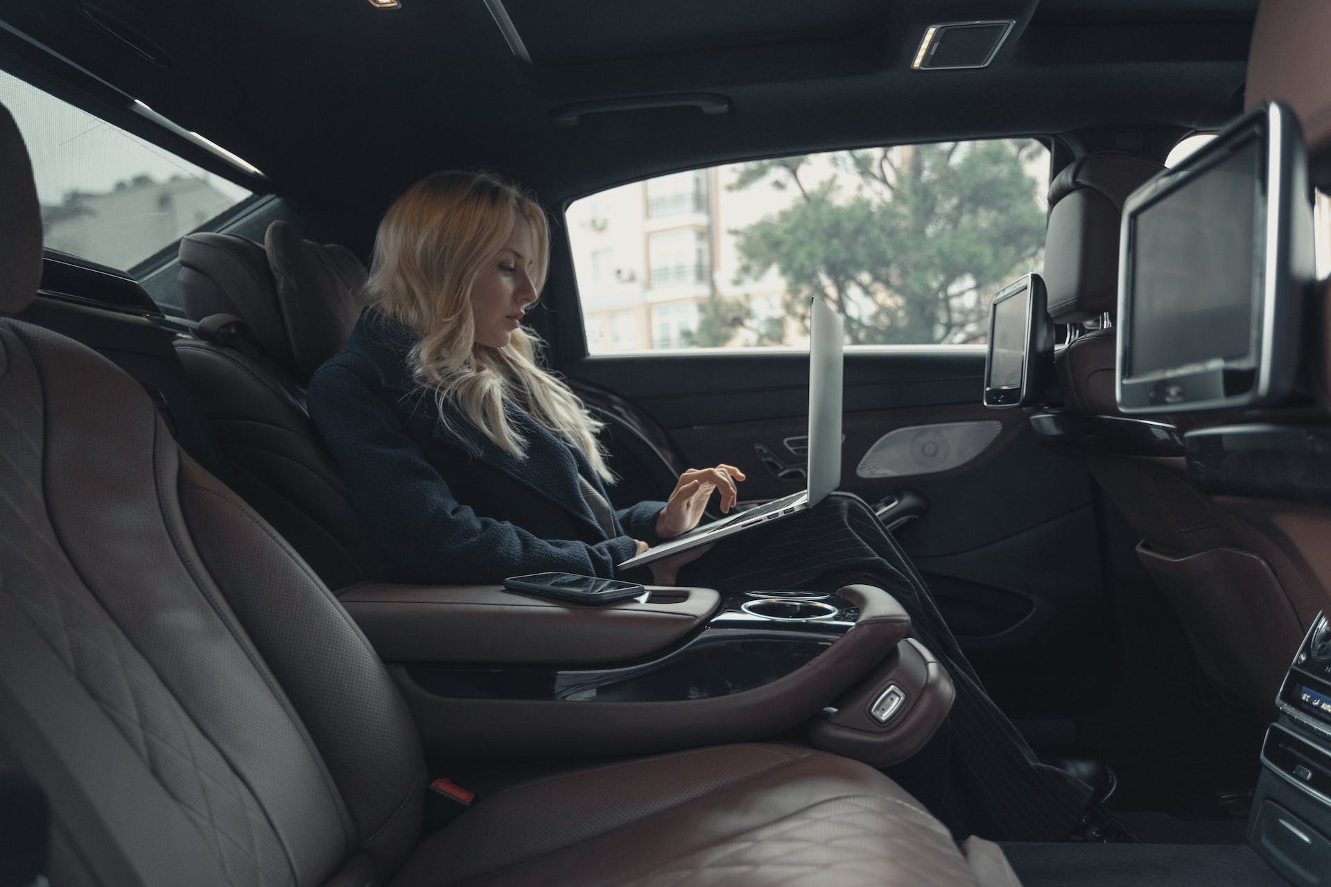 blonde vrouw werkend op een laptop achterin een taxi