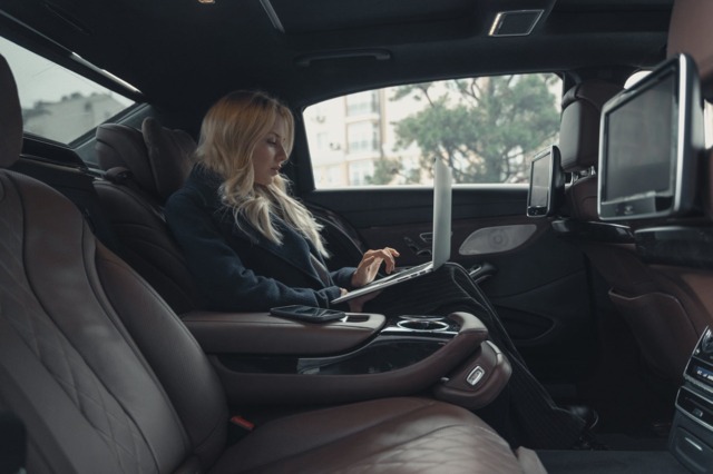 blonde vrouw werkend op een laptop achterin een taxi